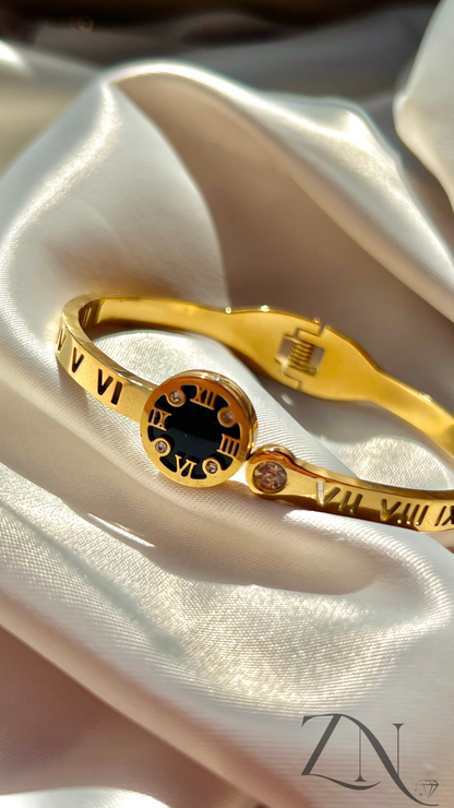 Gold-plated bangle bracelet featuring black-accented Roman numerals in a sleek circular design.