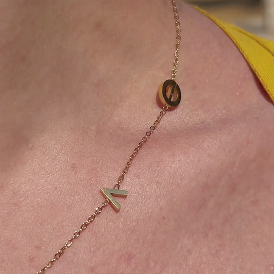 Close-up of gold L.O.V.E letter charm necklace worn layered with soft natural lighting.