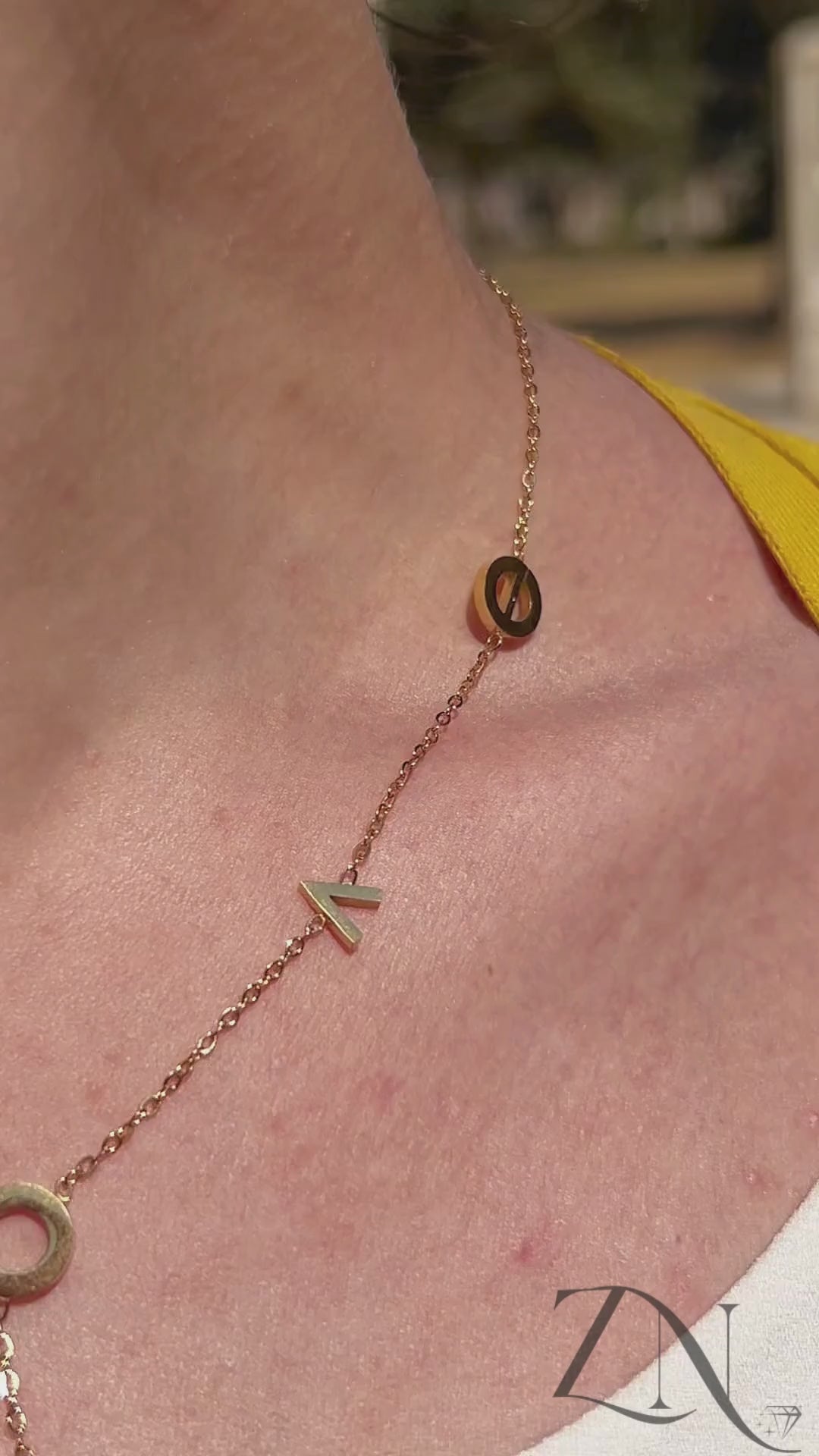 Close-up of gold L.O.V.E letter charm necklace worn layered with soft natural lighting.