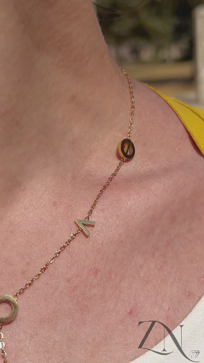 Close-up of gold L.O.V.E letter charm necklace worn layered with soft natural lighting.