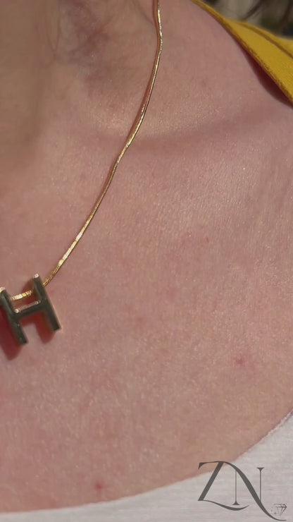Close-up of personalized heart pendant necklace with engraved initial, shown worn in soft lighting.