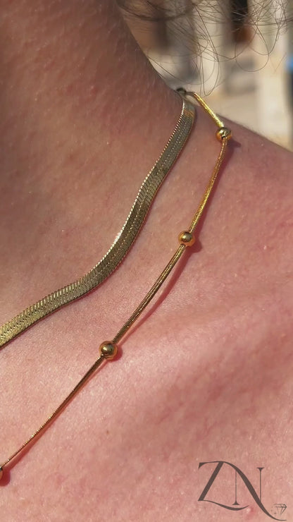 Close-up of gold serpentine and beaded necklaces worn together for a stacked look