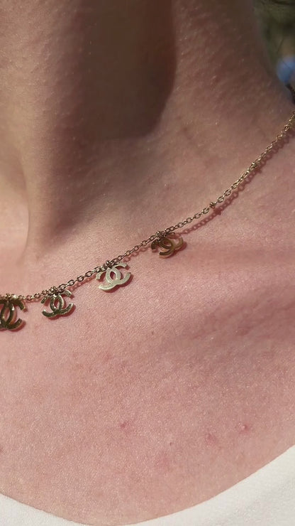 Chunky charm necklace featuring gold link chain and designer-inspired symbols, shown worn in motion.